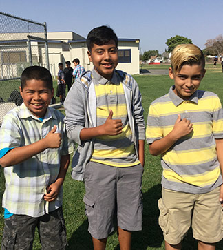Three male students pose outside as their hold thumbs up