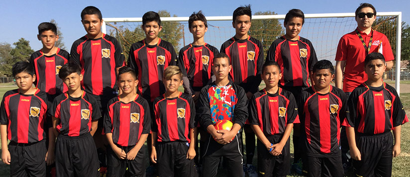 Soccer team and coach pose together in front of a soccer goal on a field